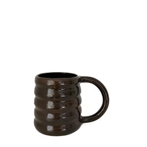 May include: A dark brown ceramic mug with a ribbed design. The mug has a rounded handle and a glossy finish. The interior of the mug is black. This handmade mug is perfect for coffee, tea, or any hot beverage.