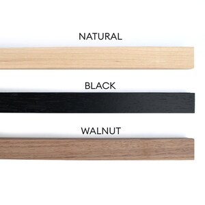 May include: Three wooden samples in natural, black, and walnut finishes. The samples are arranged vertically with the natural finish at the top, followed by the black finish, and the walnut finish at the bottom. The text "NATURAL", "BLACK", and "WALNUT" is printed below each sample.