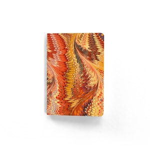 May include: A rectangular notebook with a marbled design. The cover features a swirling pattern of orange, yellow, and brown hues. The notebook is set against a white background.