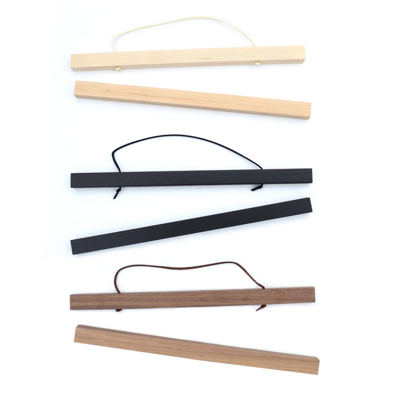 May include: Five different wooden poster hangers with black and brown cords. The hangers are made of natural wood, black wood, and walnut wood.