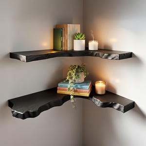 K&ouml;nnte beinhalten: Zwei schwarze Eckregale mit nat&uuml;rlicher Kante, montiert an einer hellgrauen Wand. Das obere Regal enth&auml;lt B&uuml;cher, eine Sukkulente und Kerzen. Das untere Regal hat B&uuml;cher, eine Topfpflanze und eine brennende Kerze.