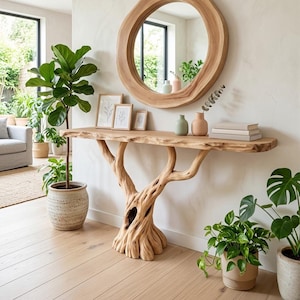 May include: A console table with a natural live-edge wooden top supported by a base crafted from a gnarled tree trunk. Above the table hangs a large round wooden-framed mirror. The table holds three small framed prints, two vases, and books.