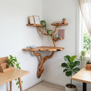 Op de afbeelding: Een unieke, houten boomvormige wandplank. De planken zijn gemaakt van natuurlijk hout en worden ondersteund door takken die uit de muur steken. De planken bevatten kleine planten, boeken en decoratieve items. De plank staat in een hoek van een kamer met een raam.