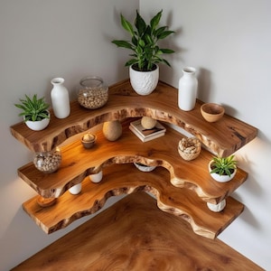 Op de afbeelding: Drie houten hoekplanken met een natuurlijk randontwerp. De planken zijn versierd met planten in witte potten, glazen potten en kleine kommen. De planken zijn gemaakt van warm getint hout. Ze zijn ontworpen voor een hoek.