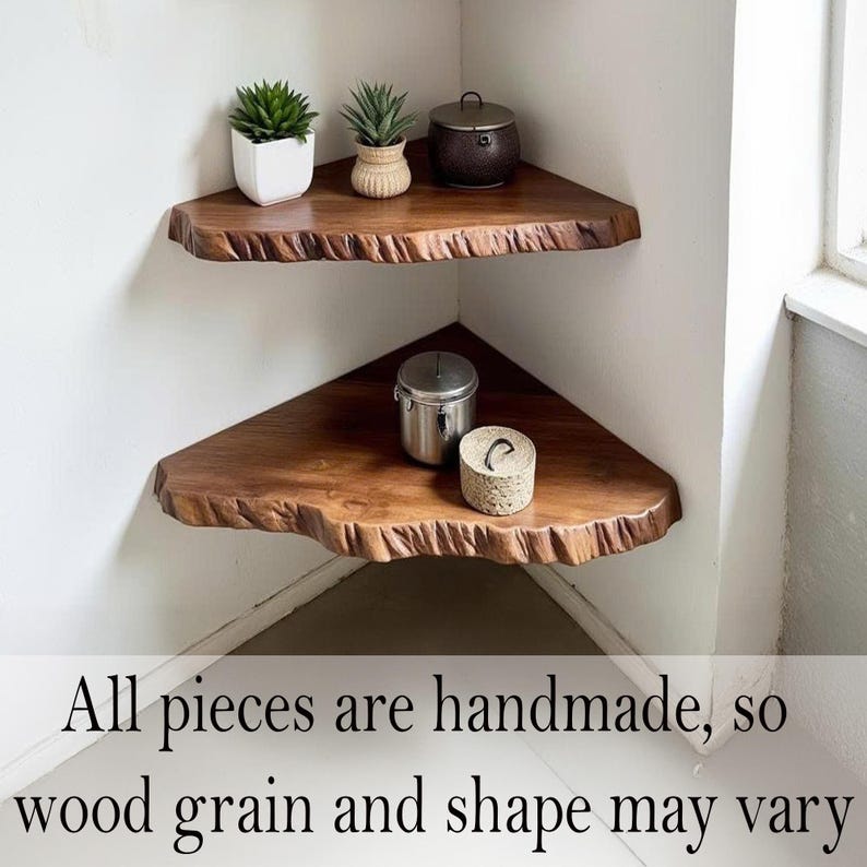 Op de afbeelding: Twee handgemaakte, driehoekige houten hoekplanken met levende randen zijn in een hoek gemonteerd. De planken zijn gebeitst in een rijke bruine kleur en bevatten kleine potplanten en decoratieve containers. De tekst onderaan luidt: "All pieces are handmade, so wood grain and shape may vary."