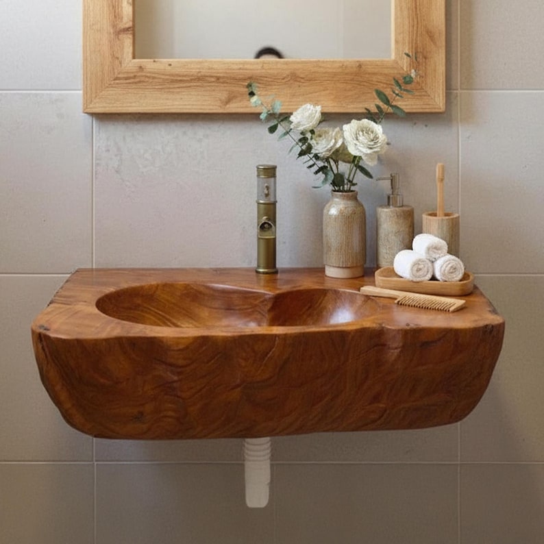 K&ouml;nnte beinhalten: Ein rustikales Badezimmerwaschbecken aus Holz mit einem geschnitzten Becken. Das Waschbecken ist an einer Wand montiert und weist eine nat&uuml;rliche Holzmaserung auf. Zubeh&ouml;r umfasst eine Vase mit wei&szlig;en Blumen, einen Seifenspender und gerollte Handt&uuml;cher.