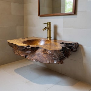 May include: A unique, floating wooden sink with a natural, organic edge. The sink is made of a rich, dark brown wood and features a round basin. A brass faucet is mounted on the sink. The sink is a bathroom fixture.