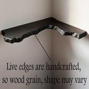 K&ouml;nnte beinhalten: Schwarzes Eckregal mit einem Design mit lebenden Kanten. Das Regal ist an einer wei&szlig;en Wand montiert. Der Text auf dem Bild lautet: "Live-Kanten sind handgefertigt, daher k&ouml;nnen Maserung und Form variieren."