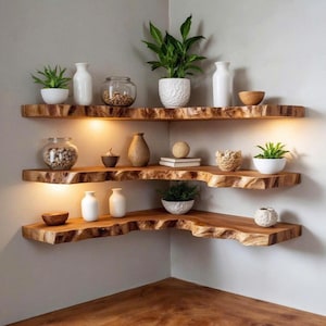 Op de afbeelding: Drie verdiepingen tellende houten hoekplanken met details van de ruwe rand. De planken tonen diverse decoratieve items, waaronder kleine potplanten, witte vazen, glazen potten en houten kommen. Warme verlichting verlicht de planken.