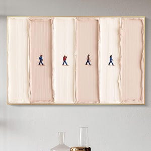May include: Abstract art piece featuring four tiny figures walking across a textured, vertical background of alternating light pink and white brushstrokes, framed in gold. The artwork hangs above a wooden table with green chairs.