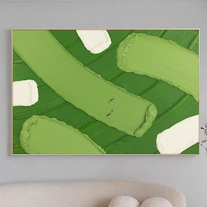 May include: Abstract art piece featuring broad brushstrokes of light and dark green, with accents of white. The painting is framed in gold and hangs on a light gray wall. The artwork is a modern, minimalist design.