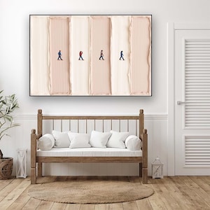 May include: Abstract art print featuring four tiny figures walking across vertical brushstrokes of varying shades of beige and cream. The artwork is framed in black and hangs above a wooden bench with white cushions.