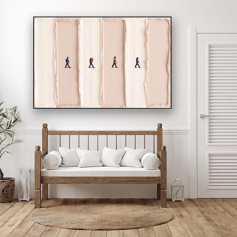 May include: Abstract art print featuring four tiny figures walking across vertical brushstrokes of varying shades of beige and cream. The artwork is framed in black and hangs above a wooden bench with white cushions.