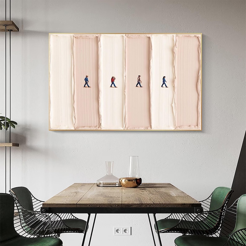 May include: Abstract art piece featuring four tiny figures walking across a textured, vertical background of alternating light pink and white brushstrokes, framed in gold. The artwork hangs above a wooden table with green chairs.