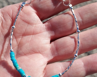 May include: A silver bracelet with a row of turquoise blue beads. The bracelet has a silver clasp.