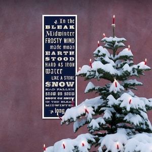 May include: A Christmas tree covered in snow with lit red candles. A navy blue sign displays the poem "In the Bleak Midwinter" in white text. The background is a muted red.