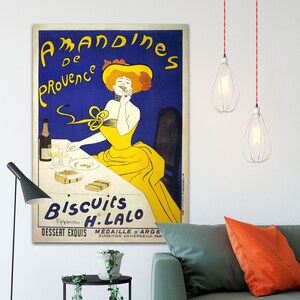 A vintage poster advertising 'Amandines de Provence' biscuits by H. Lalo. The poster features a woman in a yellow dress and a yellow hat, sitting at a table with a glass of wine and a box of biscuits. The text on the poster reads 'Amandines de Provence' 'Biscuits H. Lalo' 'Dessert Exquis' 'Médaille d'Argent Exposition Universelle, Paris'.