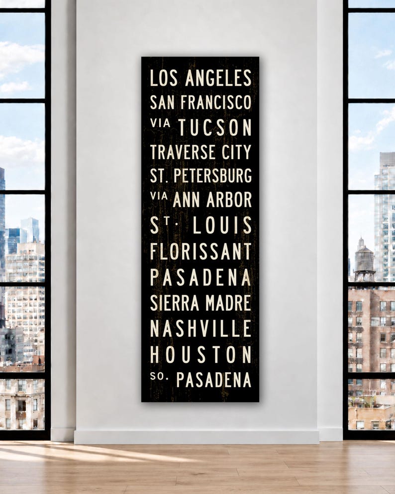 May include: A tall, rectangular black wooden sign featuring white, sans-serif text listing the cities: Los Angeles, San Francisco, via Tucson, Traverse City, St. Petersburg, via Ann Arbor, St. Louis, Florissant, Pasadena, Sierra Madre, Nashville, Houston, So. Pasadena.