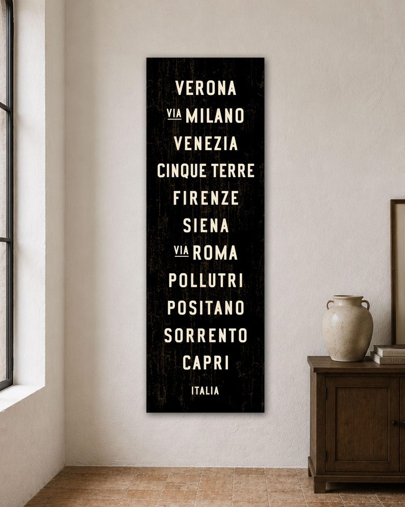 Pu&ograve; includere: Un cartello da parete nero, alto e rettangolare, con una texture usurata e testo bianco che elenca citt&agrave; italiane: VERONA, VIA MILANO, VENEZIA, CINQUE TERRE, FIRENZE, SIENA, VIA ROMA, POLLUTRI, POSITANO, SORRENTO, CAPRI e la parola ITALIA.