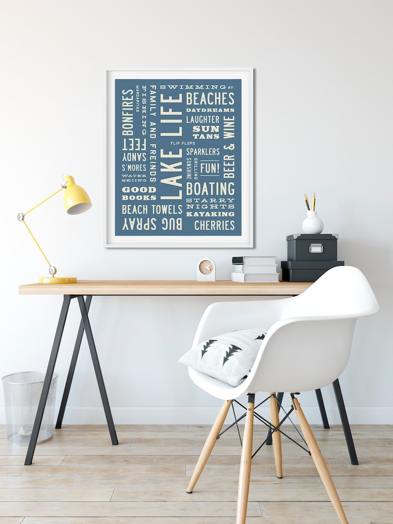 May include: A blue and white typography print with the words "Lake Life" in the center. The print features a list of words related to lake activities, such as swimming, beaches, bonfires, fishing, and boating.