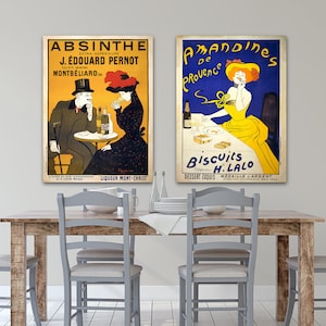 Puede incluir: Dos carteles publicitarios franceses vintage para Absenta y Almendra de Provenza. El cartel de Absenta muestra a un hombre y una mujer sentados a una mesa con una botella de Absenta. El cartel de Almendra de Provenza muestra a una mujer sentada a una mesa con un plato de galletas. Ambos carteles est&aacute;n en un ambiente de comedor con una mesa y sillas de madera.