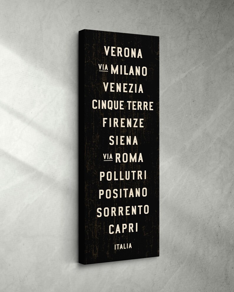 Pu&ograve; includere: Un quadro verticale rettangolare su tela nera con un elenco di citt&agrave; italiane in lettere maiuscole bianche senza grazie. Il testo recita: VERONA, VIA MILANO, VENEZIA, CINQUE TERRE, FIRENZE, SIENA, VIA ROMA, POLLUTRI, POSITANO, SORRENTO, CAPRI, ITALIA.