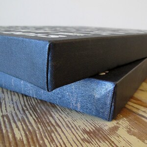May include: Two black canvas prints stacked on top of each other. The top print has white text on it. The bottom print is slightly visible underneath the top print.