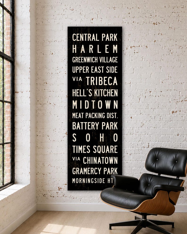 May include: A tall, rectangular black wall sign featuring white text listing New York City neighborhoods including Central Park, Harlem, Greenwich Village, Upper East Side, Tribeca, Hell's Kitchen, Midtown, Meat Packing Dist., Battery Park, Soho, Times Square, Chinatown, Gramercy Park, and Morningside Ht.