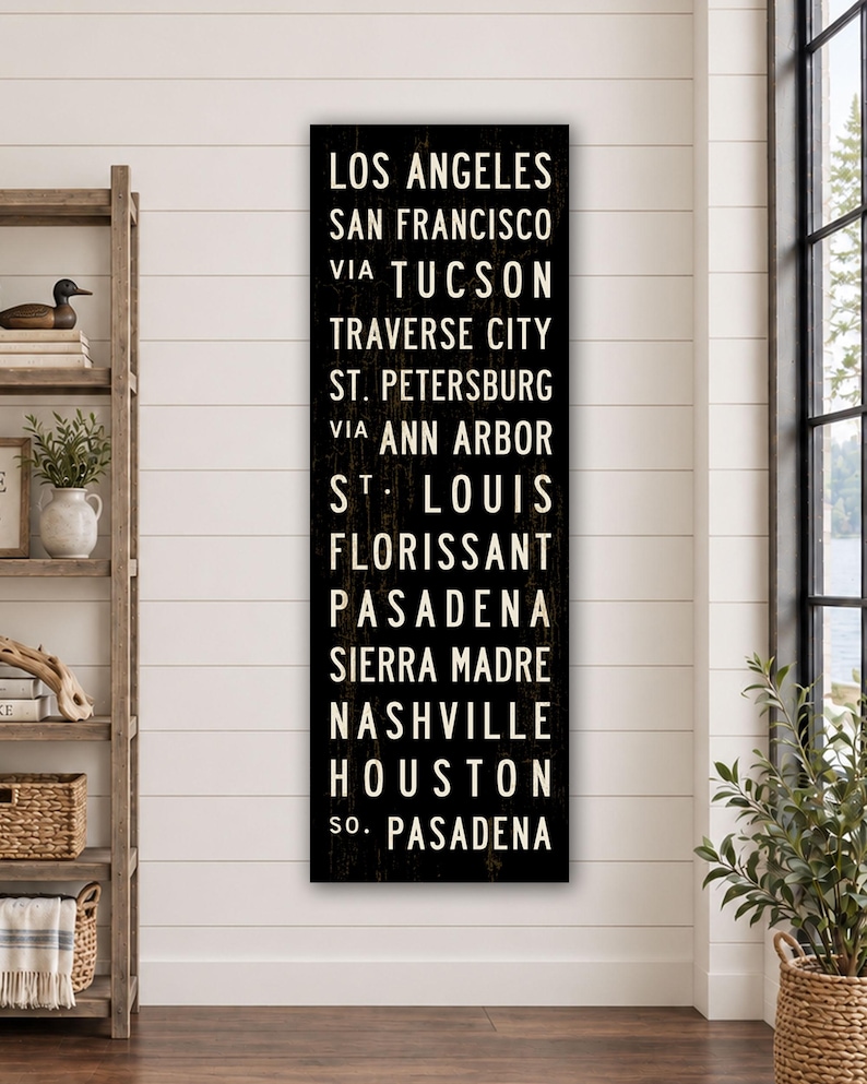 May include: A tall, rectangular black wooden sign featuring white, sans-serif text listing the cities: Los Angeles, San Francisco, via Tucson, Traverse City, St. Petersburg, via Ann Arbor, St. Louis, Florissant, Pasadena, Sierra Madre, Nashville, Houston, so. Pasadena.
