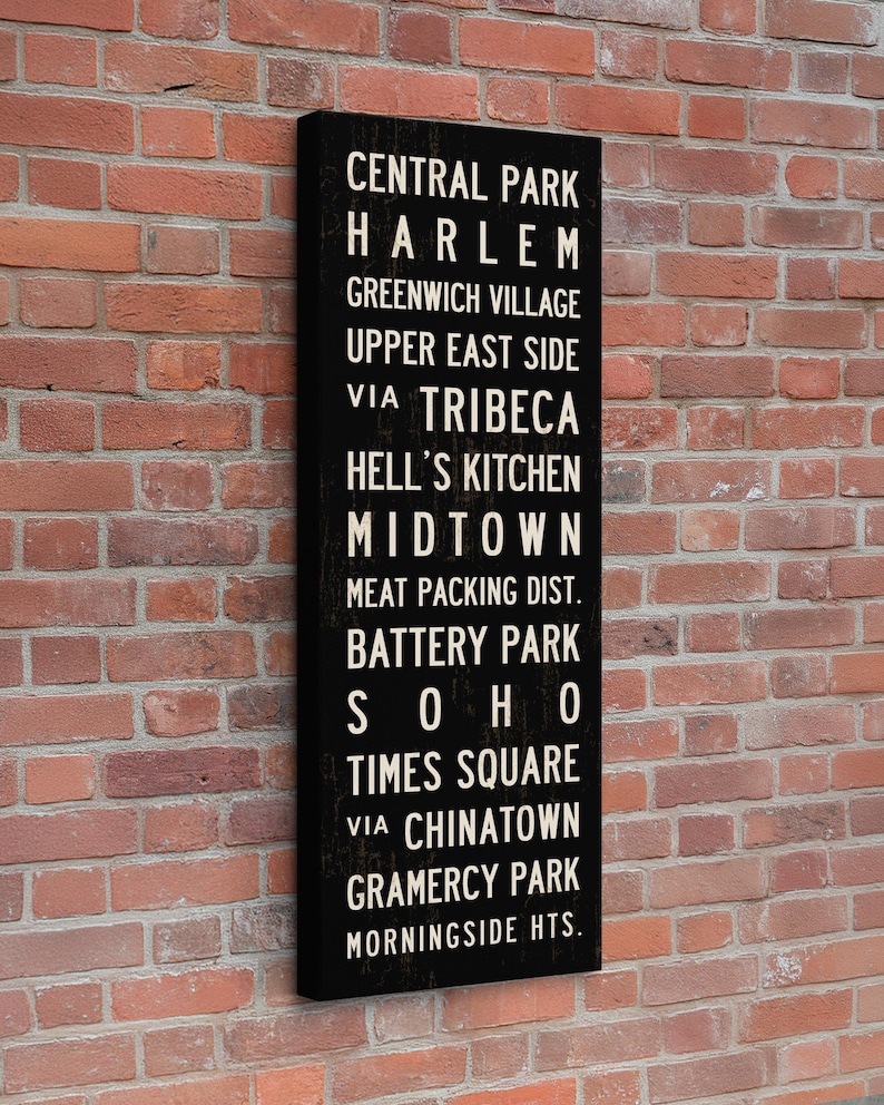 May include: A vertical rectangular black wall sign featuring white text listing New York City neighborhoods including Central Park, Harlem, Greenwich Village, Upper East Side, Tribeca, Hell's Kitchen, Midtown, Meat Packing Dist., Battery Park, Soho, Times Square, Chinatown, Gramercy Park, and Morningside Hts.