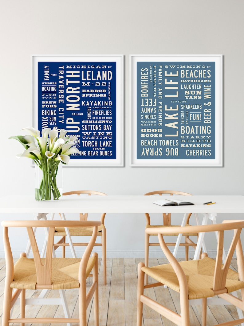 May include: Two blue and white framed prints with white text on a blue background. The left print features the words "Up North" and "Michigan" with a list of activities and places. The right print features the words "Lake Life" and "Swimming" with a list of activities and places.