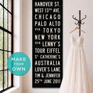 May include: A tall, rectangular black wooden sign with white text listing locations including Hanover St., West 13th Ave., Chicago, Palo Alto, Tokyo, New York, Lenny's, Tour Eiffel, St. Catherine's, Australia, Lover's Lane, and Tim & Jennifer 25th June 2011.