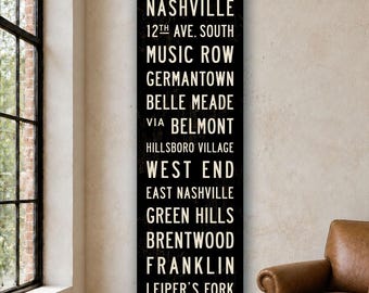 May include: A tall, rectangular black wall sign featuring white sans-serif text listing Nashville neighborhoods and locations including 12th Ave. South, Music Row, Germantown, Belle Meade, Belmont, Hillsboro Village, West End, East Nashville, Green Hills, Brentwood, Franklin, and Leiper's Fork.
