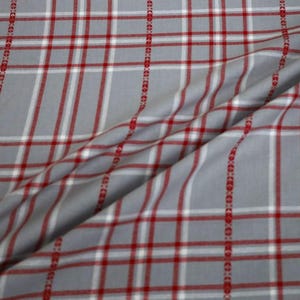 May include: Gray fabric with a plaid pattern featuring red and white lines. Vertical red dotted lines run along the fabric. The fabric is folded, showing the texture and drape of the material.