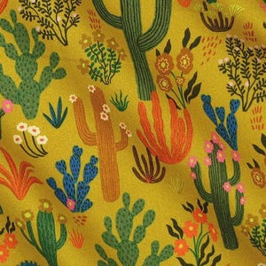May include: A fabric with a repeating pattern of cacti, flowers, and desert plants in shades of green, orange, brown, and blue on a mustard yellow background. The design features various cactus shapes and floral elements.