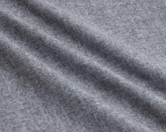 May include: Close-up of a textured, gray fabric with subtle diagonal folds. The material appears soft and has a slightly mottled appearance, suggesting a woven or knitted construction. The overall tone is neutral, with variations in light and shadow.