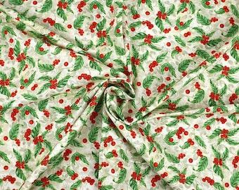 May include: A fabric with a repeating pattern of green leaves and red berries on a cream background. The fabric is folded, showing the texture and design. The pattern is reminiscent of holly.