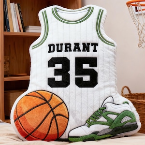 May include: A plush basketball-themed pillow set featuring a white jersey with "DURANT 35", a basketball, and a green and white sneaker. The jersey pillow is approximately 24 inches tall.