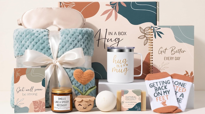 May include: A gift set featuring a light blue textured blanket with a white ribbon, a white mug with the text Hug in a Mug, a notebook labeled Get Better Every Day, a candle, a crochet heart plant, a bath bomb, soap, and socks.