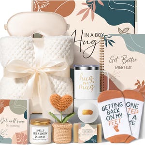 May include: A gift set containing a cream-colored textured blanket with a ribbon, a white mug with the text 'hug in a mug', a spiral notebook labeled 'Get Better EVERY DAY', a candle, a crochet heart plant, a bath bomb, soap, and socks.