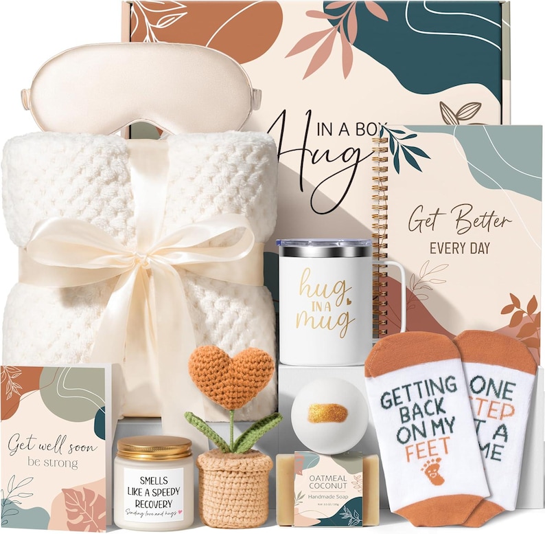 May include: A gift set containing a cream-colored textured blanket with a ribbon, a white mug with the text 'hug in a mug', a spiral notebook labeled 'Get Better EVERY DAY', a candle, a crochet heart plant, a bath bomb, soap, and socks.