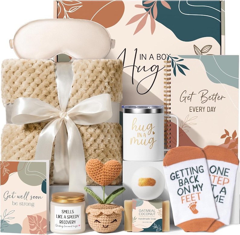 May include: A gift set containing a beige textured blanket with a white ribbon, a sleep mask, a white mug with the text 'hug in a mug', a notebook labeled 'Get Better EVERY DAY', a crochet heart plant, a candle, soap, and socks with the text 'GETTING BACK ON MY FEET ONE STEP AT A TIME'.