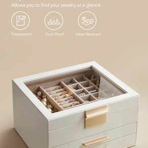 May include: A white jewelry storage box with a clear window, featuring multiple compartments. The box has a gold-coloured clasp and drawer pulls. Text on the image reads "Stylish Clear Window" and "Allows you to find your jewelry at a glance."