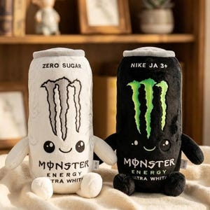 May include: Two plush toys shaped like energy drink cans. The left one is white with the text ZERO SUGAR and MONSTER ENERGY ULTRA WHITE. The right one is black with the text NIKE JA 3+ and MONSTER ENERGY ULTRA WHITE. Both have arms, legs, and faces.