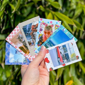 Puede incluir: Seis marcos de fotos instantáneas coloridos con diferentes diseños. Los marcos están decorados con corazones, fresas, estrellas y temas náuticos. Los marcos se sostienen en una mano.