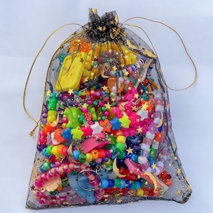 May include: A black mesh drawstring bag filled with colorful beaded jewelry and accessories. The bag is adorned with gold stars and a gold drawstring. The contents include bracelets, star-shaped charms, and other decorative items in various bright colors.