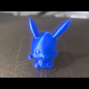 Puede incluir: Figura de conejo de dibujos animados azul brillante, impresa en 3D. El conejo tiene orejas largas y está de pie. La figura es de plástico y tiene un acabado liso y brillante. Aproximadamente 5 cm de altura.