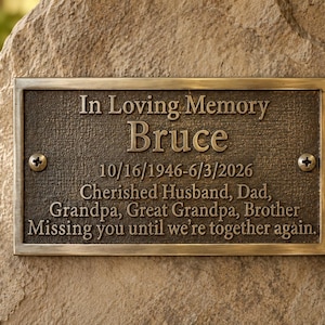 May include: A rectangular bronze memorial plaque with a textured surface, featuring the engraved text In Loving Memory Bruce 10/16/1946-6/3/2026 Cherished Husband, Dad, Grandpa, Great Grandpa, Brother Missing you until we're together again, secured by two screws.