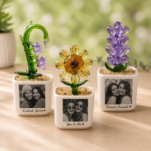 May include: Three white square ceramic planters containing glass flowers. The left planter features a green glass vine with purple accents and the text Kindred Spirits. The center planter has a yellow glass sunflower and the text You & Me. The right planter holds a purple glass flower and the text Forever Friends. Each planter displays a black and white photograph of two people.
