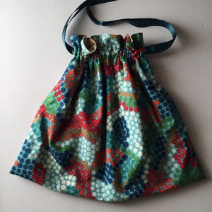 May include: A blue drawstring bag with a colorful polka dot pattern in shades of red, green, and white. The bag has a navy blue ribbon drawstring.